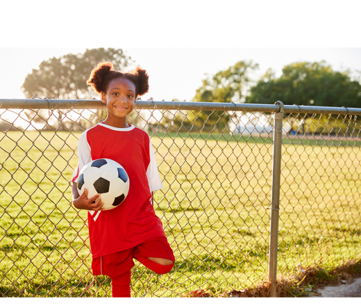 girl holding a soccer ball next to a fence